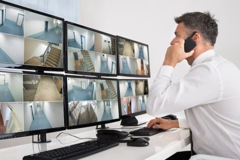 Side view of security system operator using walkie-talkie while looking at CCTV footage